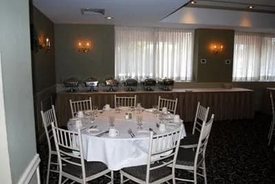 A round banquet table set for a celebration beside a chafing-dish buffet line in The Manor Inn banquet room.
