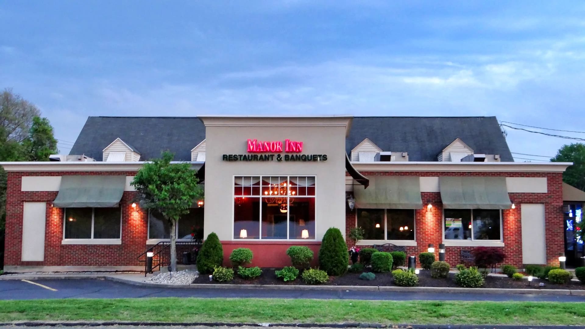 The Manor Inn at dusk — brick storefront lit by its neon Restaurant & Banquets sign, with a chandelier glowing through the front window, in Plantsville, Connecticut