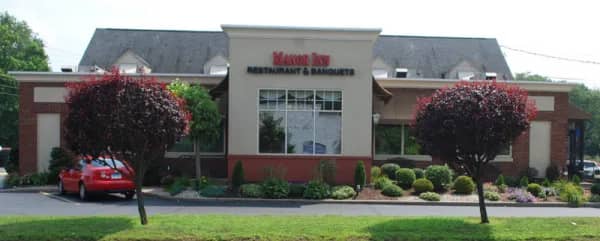 The Manor Inn's brick storefront with its lit Restaurant & Banquets sign and flanking red maple trees in Milldale, Connecticut