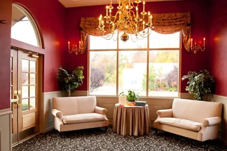 The Manor Inn's deep-red foyer lounge with a gold chandelier, arched window, and settees