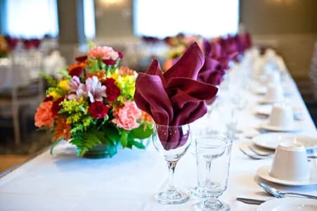 A long banquet table set with burgundy fan-folded napkins and a floral centerpiece in The Manor Inn banquet room.
